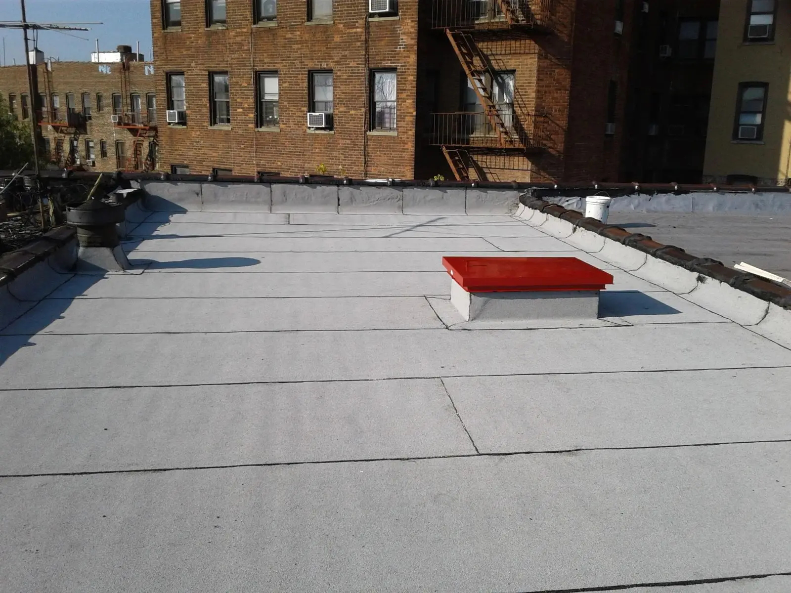 A finished flat roof on a Brooklyn row building, with brick apartment buildings behind it